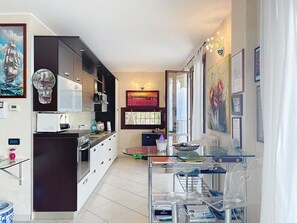 A modern kitchen with a dining area, featuring a glass table, a built-in oven, and a large clock. - Riflesso del Lario by Interhome (Bellano)