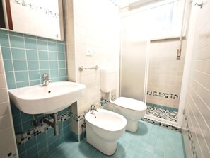 Baño con lavamanos, dos inodoros y zona de ducha.