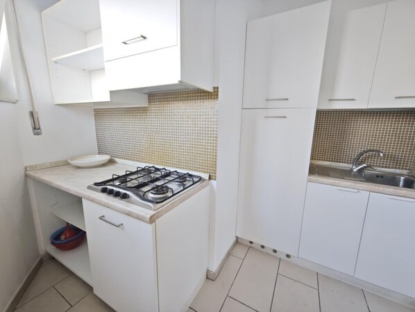 Una cocina con armarios blancos, estufa a gas, lavamanos y salpicadero de azulejos.