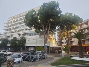 A multi-story hotel with a modern design, featuring balconies and a parking area with cars. - Cozy beachside vacation flat in Lignano (Lignano Sabbiadoro)