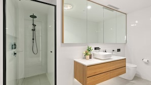 Un baño moderno con cabina de ducha de vidrio, tocador de madera con lavamanos y un espejo grande sobre el tocador.