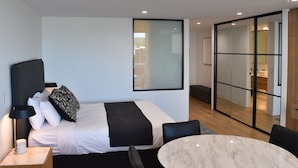 Una habitación de hotel moderna con cama, mesita de noche, lámpara y una mesa de mármol.