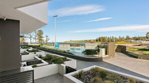 A modern outdoor pool area with a clear view of the sea, surrounded by landscaped gardens and contemporary architecture. - Kove Apartment - G03 (Kiama)