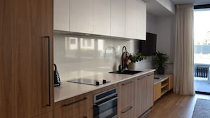 Una cocina moderna con armarios de madera, horno empotrado, pileta negra y una planta en maceta.