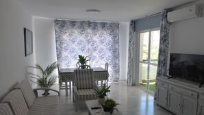 A living room with a sofa, a dining table with chairs, a TV, and a potted plant. - Lovely 1-bedroom Apartment in Roquetas de Mar, Spain (Roquetas de Mar)