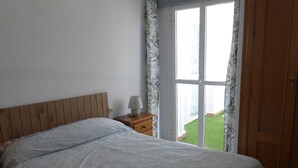 A bedroom with a bed, a nightstand, a lamp, and a view of a green lawn through a window. - Lovely 1-bedroom Apartment in Roquetas de Mar, Spain (Roquetas de Mar)