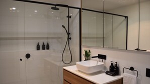 A modern bathroom with a large mirror, a white sink, and a shower area. - Kove Apartment - G05 (Kiama)