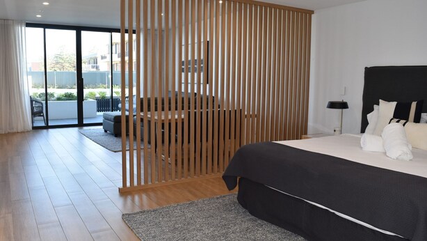 A modern hotel room with a large bed, a balcony, and a sliding wooden partition. - Kove Apartment - G05 (Kiama)