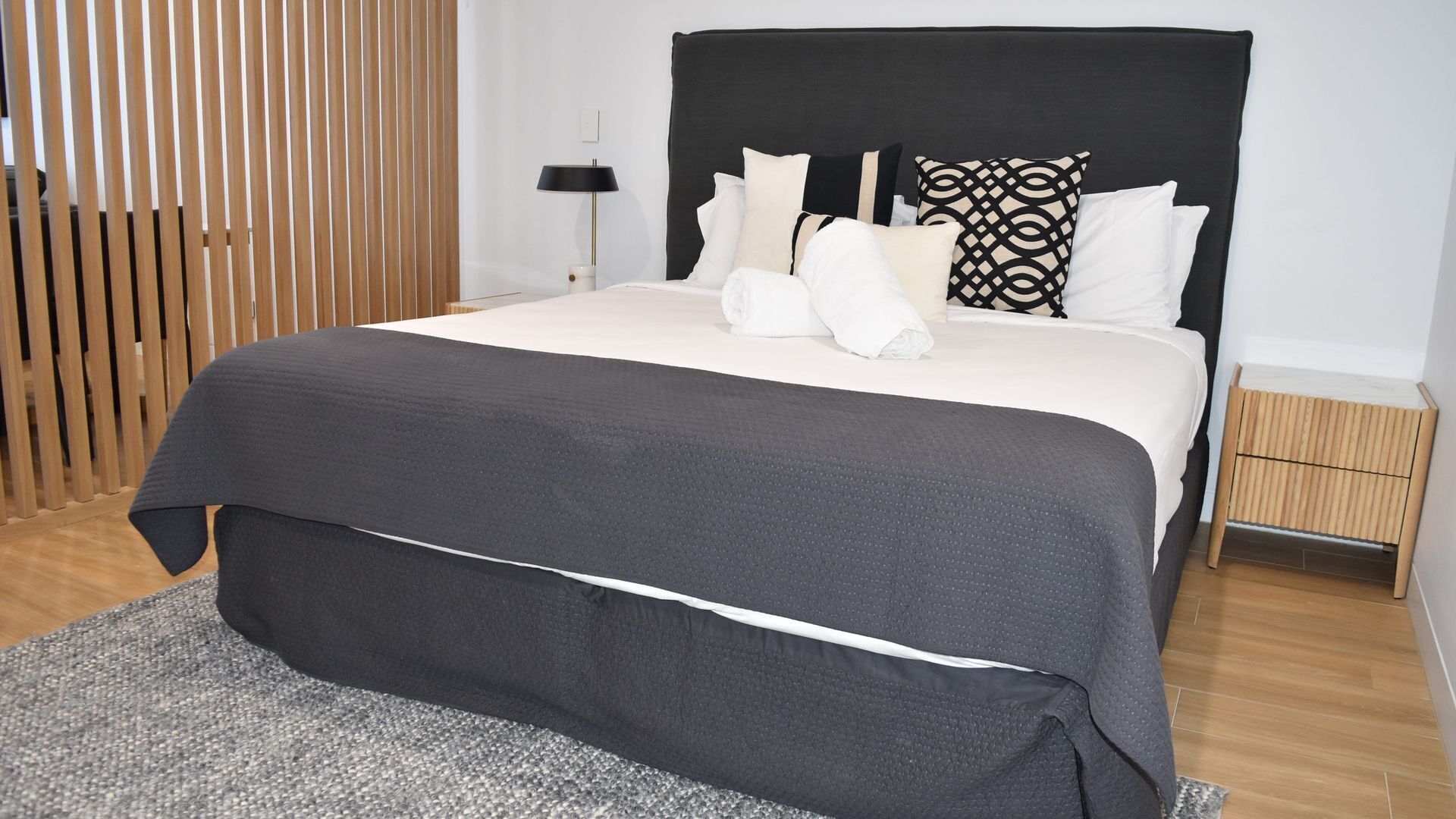 A neatly made bed with a black headboard, white pillows, and a grey throw.