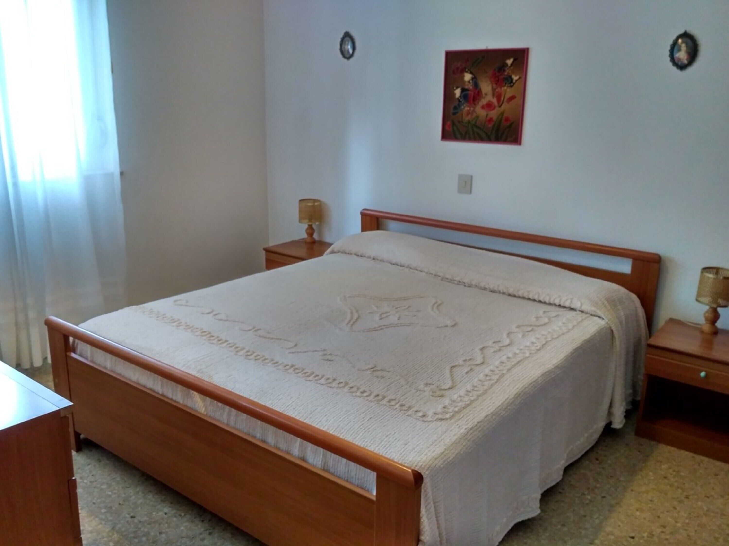 Une chambre à coucher avec un lit en bois, deux tables de chevet avec des lampes, un tableau accroché au mur et une fenêtre avec des rideaux.