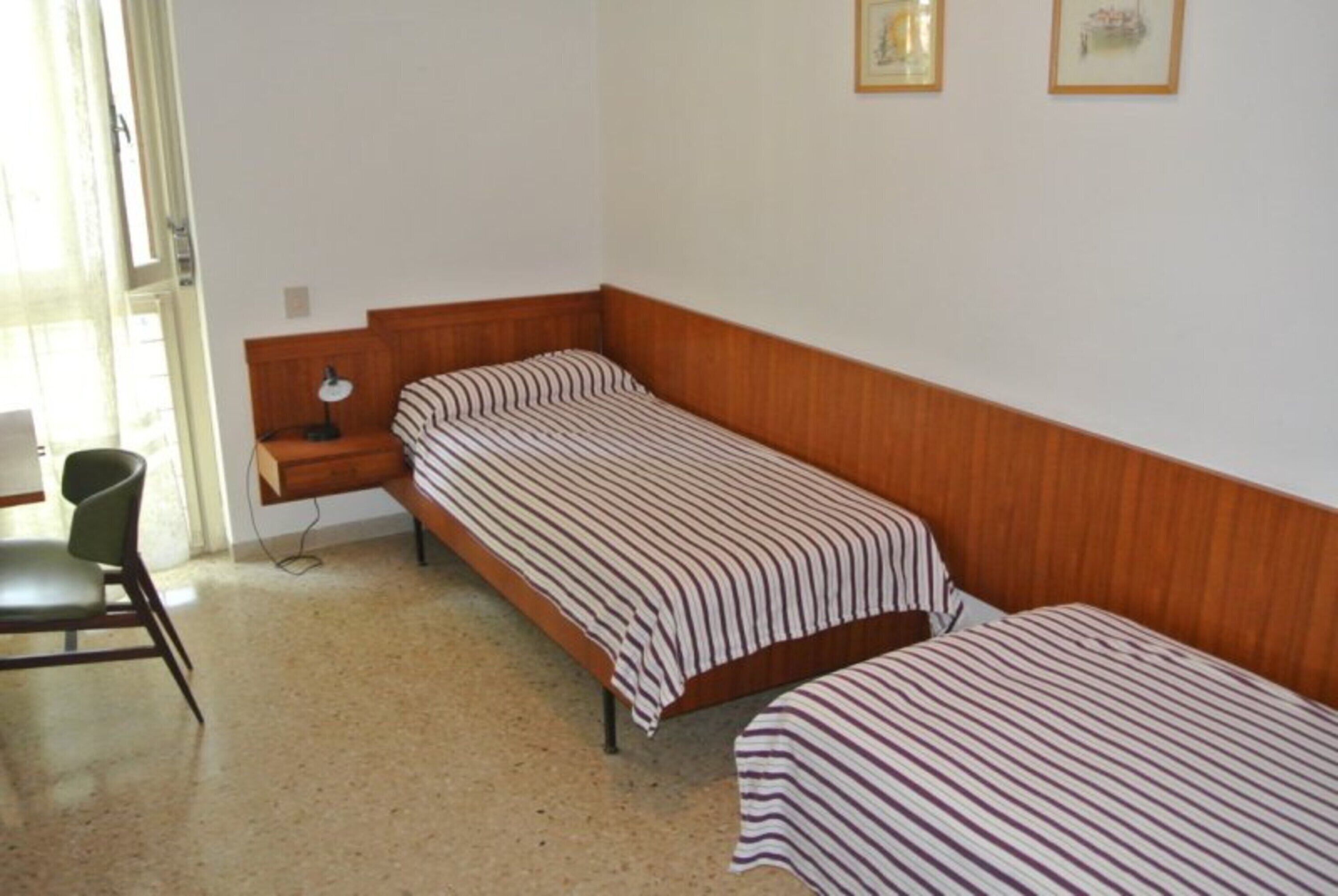 Una habitación individual con dos camas, una silla, un escritorio y una lámpara.