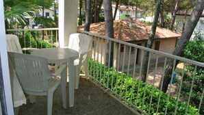 Ein Balkon mit Tisch und Stühlen, umgeben von Grünpflanzen und Blick auf ein Gebäude mit Ziegeldach.