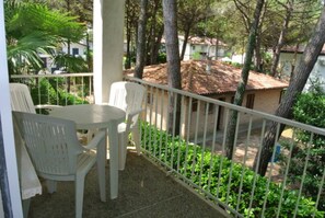 Ein Balkon mit Tisch und Stühlen, umgeben von Grünpflanzen und Blick auf ein Gebäude mit Ziegeldach.