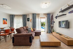 A modern living room with a sofa, coffee table, TV, and a dining area with chairs and a table.