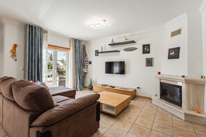 A living room with a sofa, TV, fireplace, and a view through the glass door.