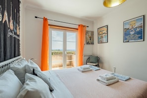 Une chambre à coucher avec un lit, une chaise, une fenêtre avec des rideaux et des œuvres d’art murales.