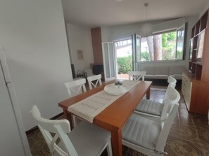 A dining area with a wooden table, white chairs, and a bench. - Relaxing holiday property with garden and parking (Lignano Sabbiadoro)