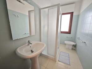 Ein Badezimmer mit einem Standwaschbecken, einer Toilette, einer Dusche und einem Fenster.