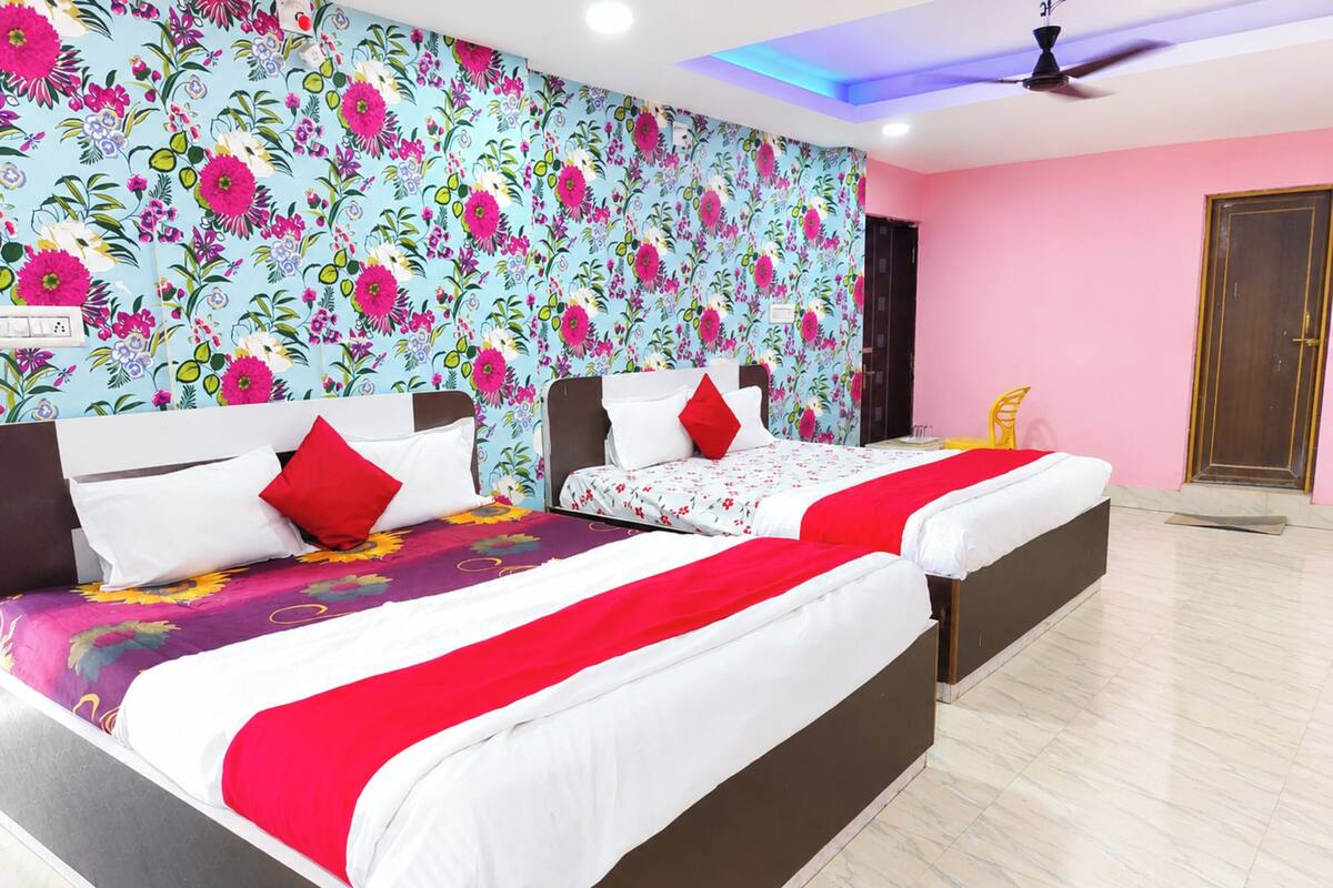 Habitación de hotel con dos camas, papel tapiz floral, ventilador de techo y una pared rosa.
