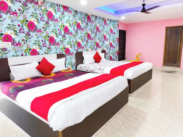 Une chambre d’hôtel avec deux lits, un papier peint à motifs floraux, un ventilateur de plafond et un mur rose.