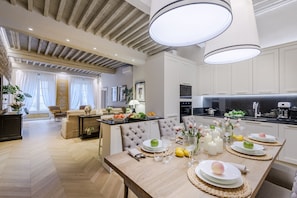 Eine moderne Küche mit weißen Schränken, ein Essbereich mit einem Holztisch, der für eine Mahlzeit gedeckt ist, und ein Wohnzimmer mit einer Couch und Vorhängen.