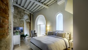 Un dormitorio con una cama grande, televisión, una silla y un escritorio con una planta.