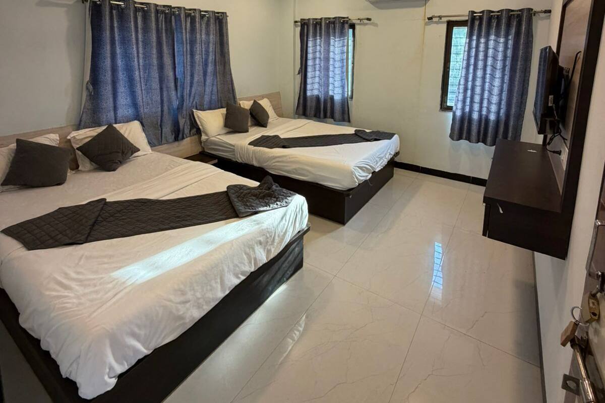 Habitación de hotel con dos camas, ventilador de techo, unidad de aire acondicionado y televisor en la pared.