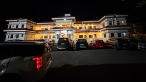 A multi-story hotel with a central entrance, parking lot, and several cars parked in front.