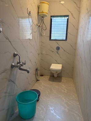 A bathroom with marble walls, a toilet, a shower with a hose, a bucket, and a window. - Hotel Majestic Inn (Ellora)