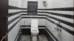 A small, tiled bathroom with a toilet, a shower, and a blue bucket on the floor.