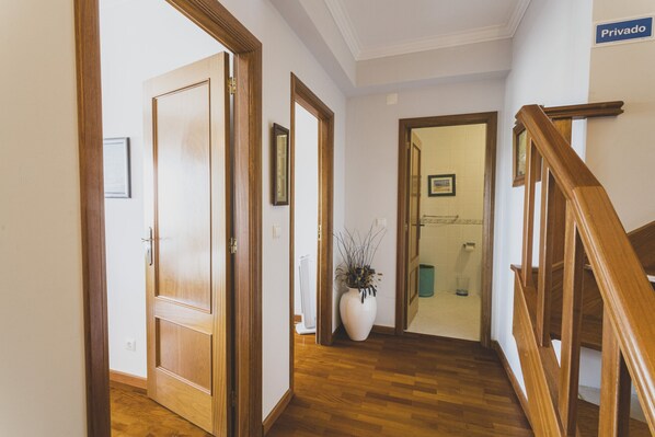 Ein Korridor mit Holztüren, einer weißen Vase mit Pflanzen und einer Treppe mit Holzhandläufen.