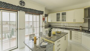 Een keuken met een granieten aanrecht, witte kastjes, een klok en een uitzicht door de glazen deur.