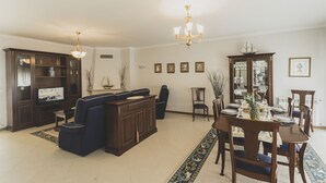 Een ruime woonkamer met een donkerblauwe bank, een houten eettafel voor vier personen, en een kroonluchter.