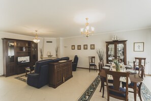 Ein geräumiges Wohnzimmer mit einem dunkelblauen Sofa, einem Holzessttisch für vier Personen und einer Kristallleuchter.