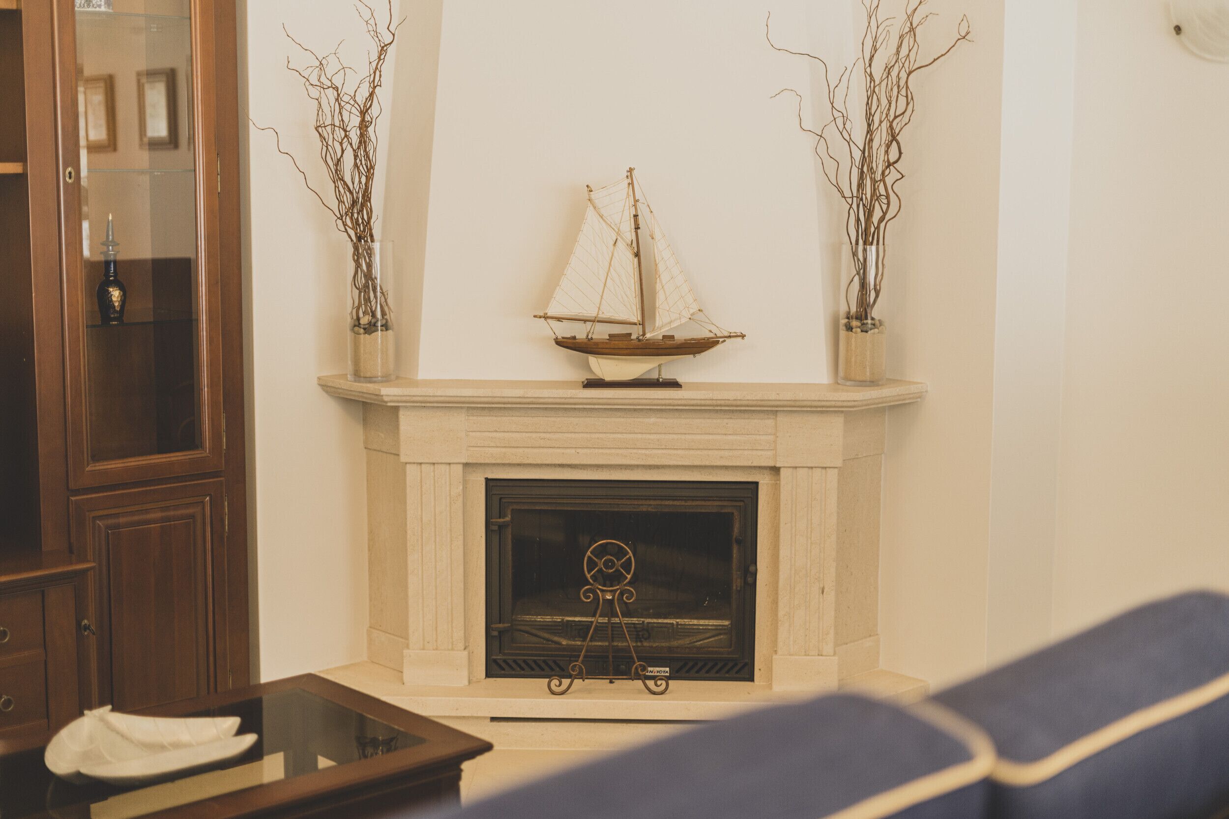Un salon avec une cheminée, une maquette de bateau et deux vases ornés de branches.