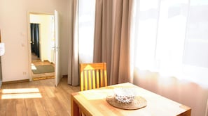Ein Zimmer mit einem Holztisch, einem gewebten Korb und einem Stuhl. Eine Tür führt in einen weiteren Raum.