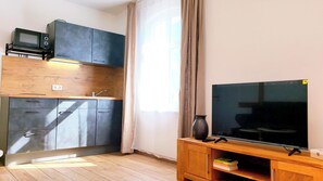 Un espai vital reduït amb cuineta, televisió de pantalla plana i un armari de fusta.