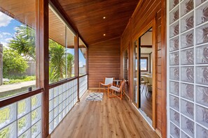 A wooden balcony with a view of greenery, a table with chairs, and a glass door.