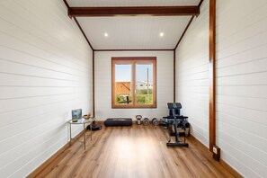 Une pièce aux murs recouverts de panneaux blancs, dotée d’un plancher en bois, d’une fenêtre offrant une belle vue et d’appareils de musculation.