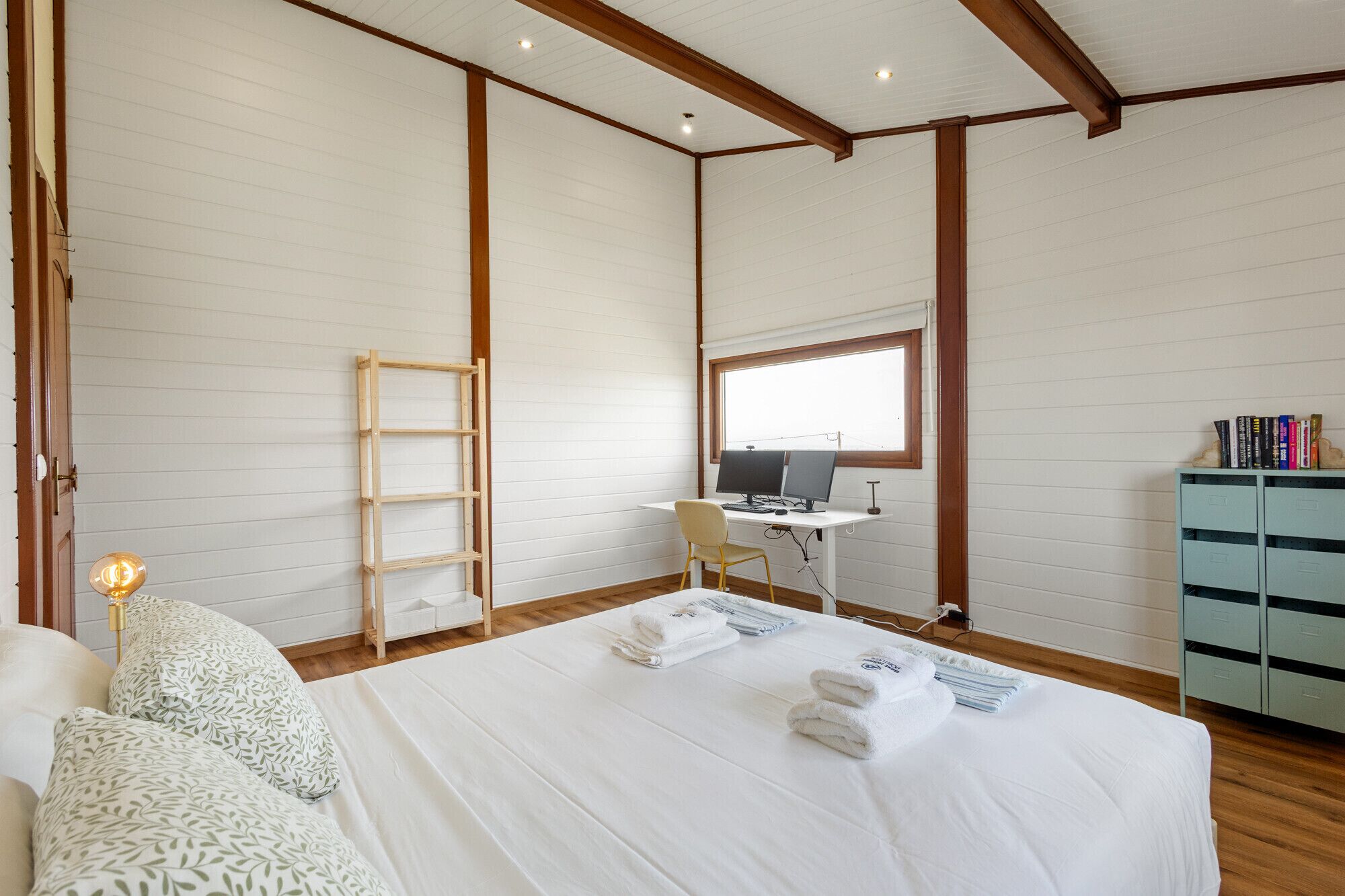 Une chambre à coucher avec un lit, un bureau avec un ordinateur, une échelle et une armoire.