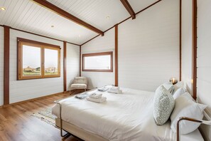 A bedroom with a bed, two windows, a chair, and a bedside table.