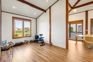 A spacious room with a wooden floor, a large window with a view, a ceiling fan, and a dining area with chairs.