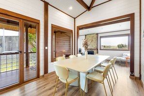 A spacious dining area with a large table and chairs, wooden beams on the ceiling, and a stone fireplace.