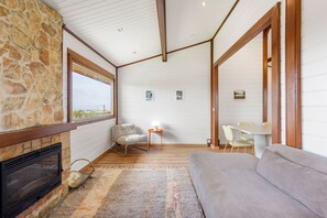 A cozy room with a stone fireplace, a sofa, a dining table with chairs, and a view through a large window.