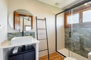 Une salle de bain avec un lavabo blanc, un miroir, une serviette, une cabine de douche en verre et une porte en bois.