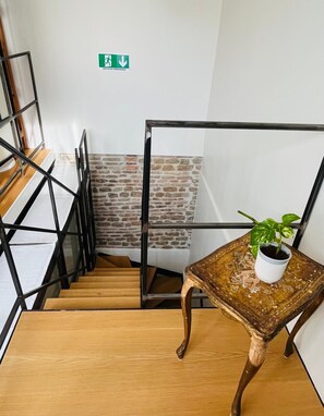 A staircase with a metal railing, a wooden floor, and a potted plant on a small table. - Torre Tolomei Trastevere (Rome)