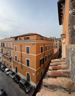A multi-story building with a uniform facade, a narrow street, and parked cars. - Torre Tolomei Trastevere (Rome)