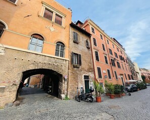 A cobblestone street with historic buildings, a narrow passageway, and parked scooters. - Torre Tolomei Trastevere (Rome)