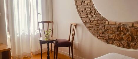 Une chambre d’hôtel avec un lit, un miroir rond, un mur en briques, une chaise et une table sur laquelle se trouve une plante.