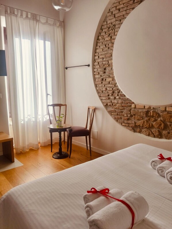 A hotel room with a bed, a round mirror, a brick wall, a chair, and a table with a plant. - Torre Tolomei Trastevere (Rome)
